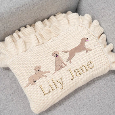 Cream personalized baby blanket with embroidered labrador retrievers and 'Lily Jane' on a gray surface