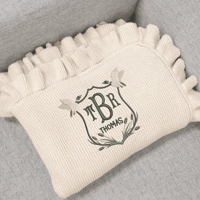 Cream personalized baby blanket with monogram mallard duck crest design on a gray surface