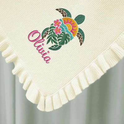 Cream personalized baby blanket with a colorful sea turtle design and the name 'Olivia' on a light gray background