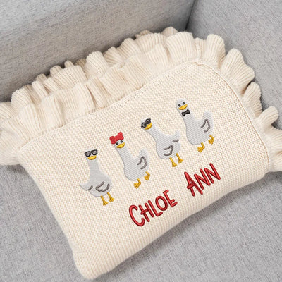 Cream personalized baby blanket with embroidered geese and text 'Chloe Ann' on a gray surface