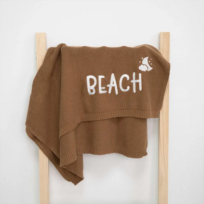 Mocha personalized baby blanket with 'BEACH' text on a wooden ladder against a white background