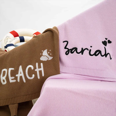 Two personalized baby blankets, one brown with 'BEACH' and one pink with 'Zariah', on a white background.