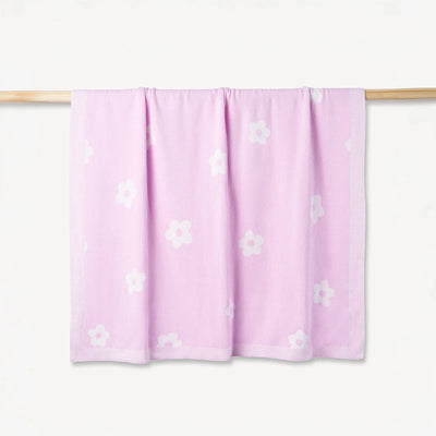 Pink blanket with white floral patterns on a wooden rod against a white background