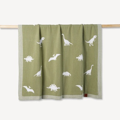 Green blanket with white dinosaur patterns on a wooden rod against a white background