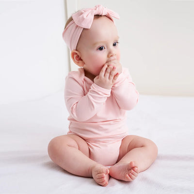Baby in a pink outfit with a matching headband sitting on a white surface.