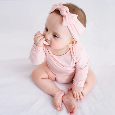 Baby wearing a pink onesie and headband on a white background