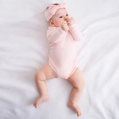 Baby in a pink onesie and headband lying on a white surface