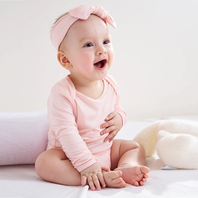 Baby in a pink outfit and headband sitting on a white surface.