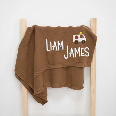 Mocha personalized baby blanket with 'Liam James' and an ambulance on a wooden frame against a white background