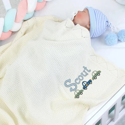 Baby wrapped in a personalized blanket with 'Scout' embroidered on it, surrounded by baby toys.