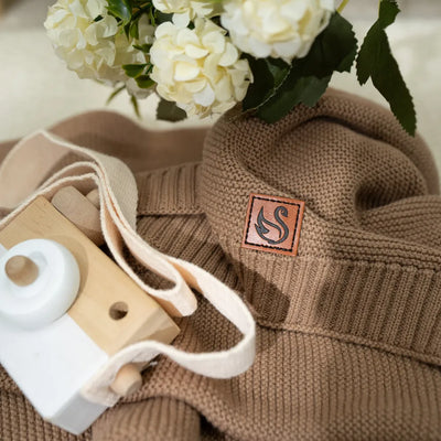 Mocha personalized baby blanket with a SWaddle AN logo patch, wooden camera, and white flowers in the background