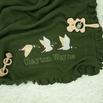 Forest green baby blanket with embroidered mallard ducks and 'Clayton Wayne' text, accompanied by a wooden toy on a white background.