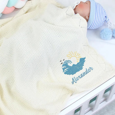 Baby wrapped in a blanket with a personalized ocean waves design and name 'Alexander'.