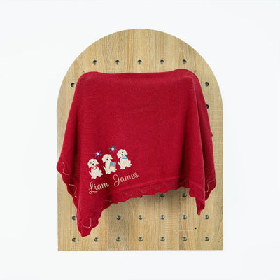 Red perosnalized baby blanket with embroidered patriotic puppy trio design and text on a wooden surface