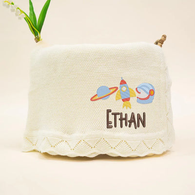 Cream personalized baby blanket with embroidered space-themed design and name 'Ethan' on a beige background