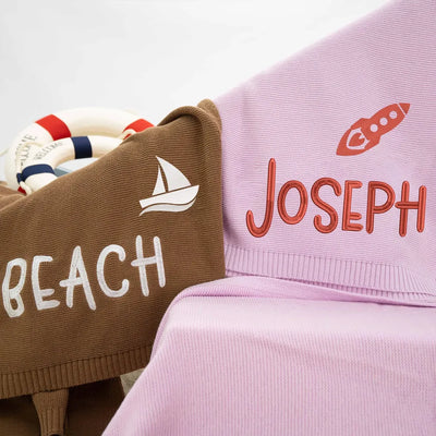 Personalized baby blanket with 'JOSEPH' embroidered on it next to a brown ones with 'BEACH' text.
