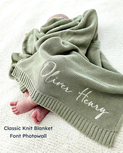 Sage green personalized blanket with 'Oliver Henry' embroidery on a baby lying underneath.