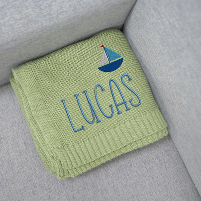Sage green baby blanket with 'Lucas' and a sailboat design on a gray surface