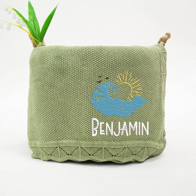 Sage green personalized baby blanket with embroidered oceanwaves design and 'Benjamin' text on a white background