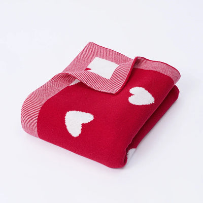Folded red blanket with white heart patterns on a light gray background