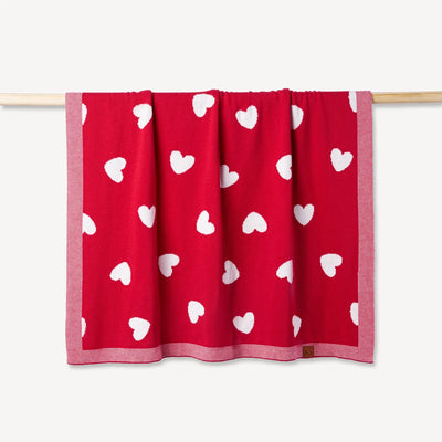 Red blanket with white heart patterns hanging on a wooden rod against a white background